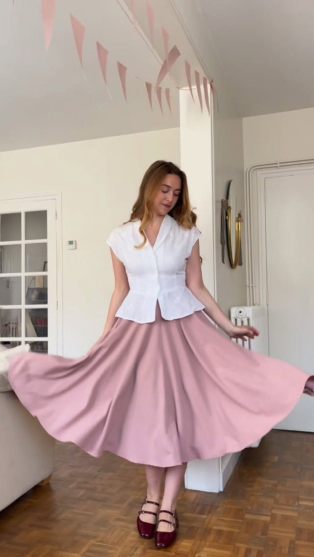 13 Going on 30 Outfits: 6 Ideas to Recreate the Iconic Style 5 Woman in a white sleeveless top and flared blush pink midi skirt posing indoors.