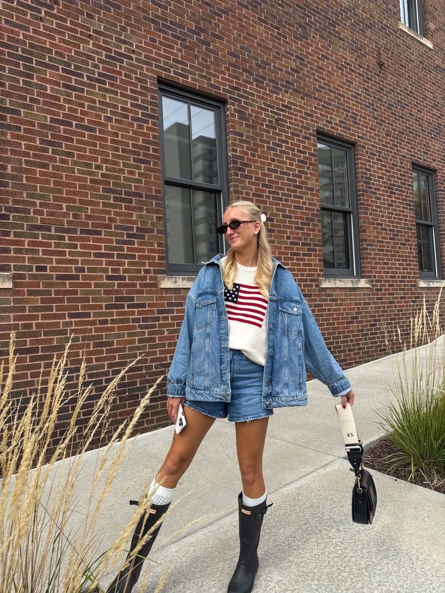 4th of July Outfits: 8 Festive Looks for Women 1 Woman wearing an American flag sweater, denim jacket, shorts, and black rubber boots.
