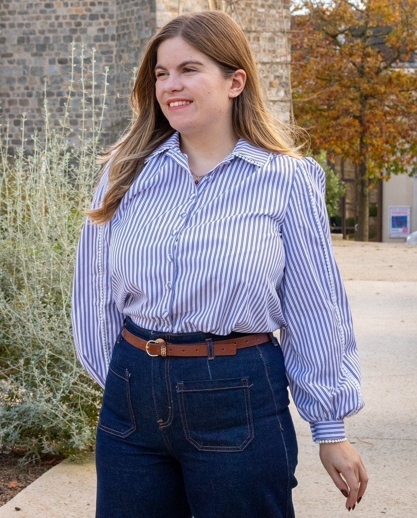 Woman in a blue striped button-down shirt and high-waisted dark denim jeans outdoors.