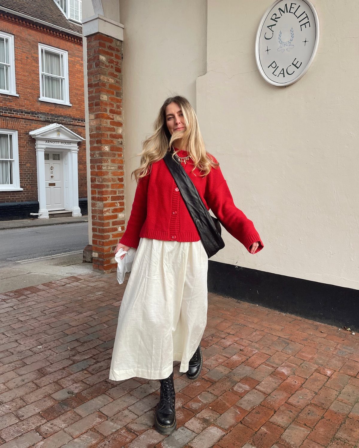 Woman wearing a red cardigan and long white skirt on a brick sidewalk