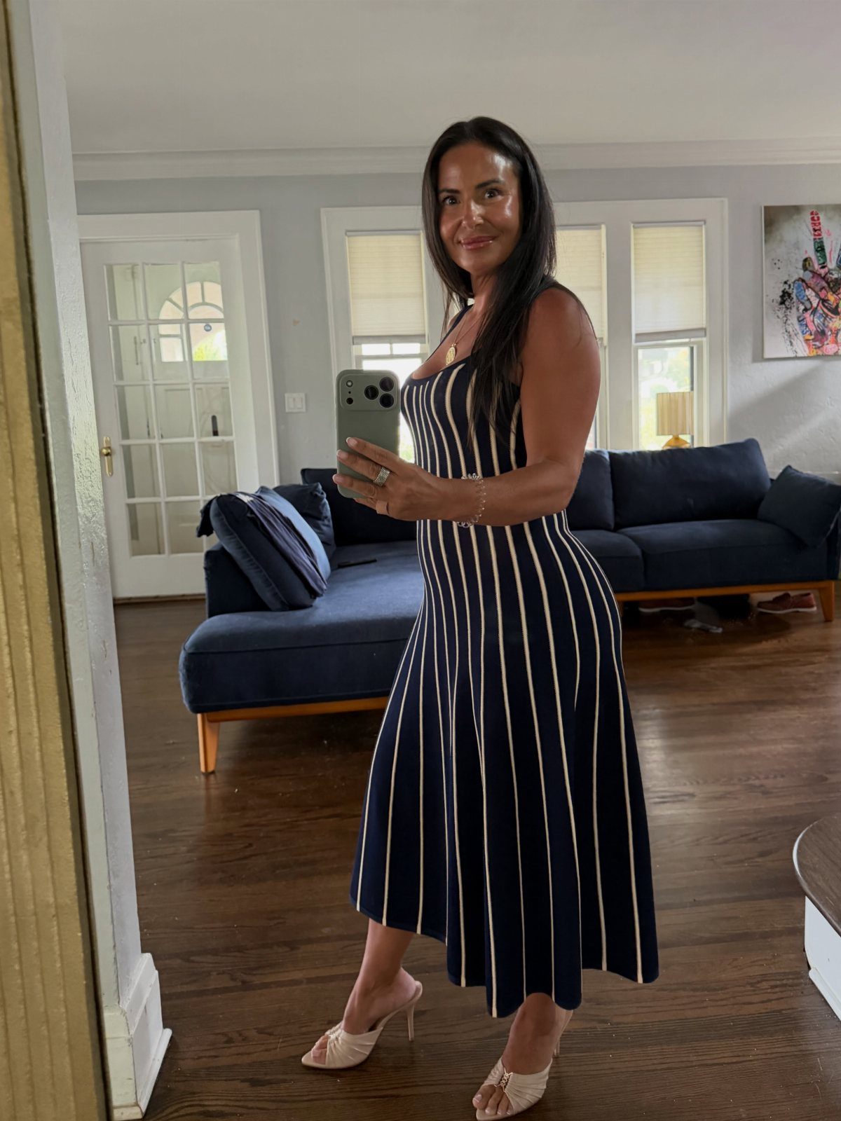 Woman in a navy blue striped midi dress and beige heels taking a selfie.