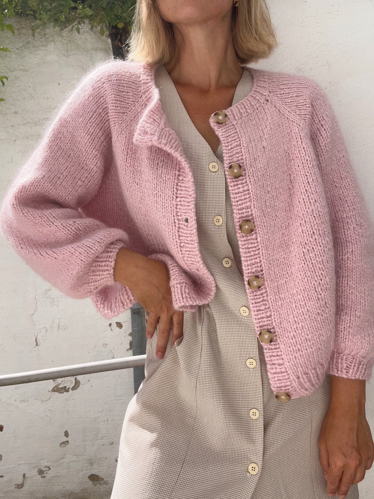 Woman wearing a light pink knit cardigan over a beige button-down midi dress.