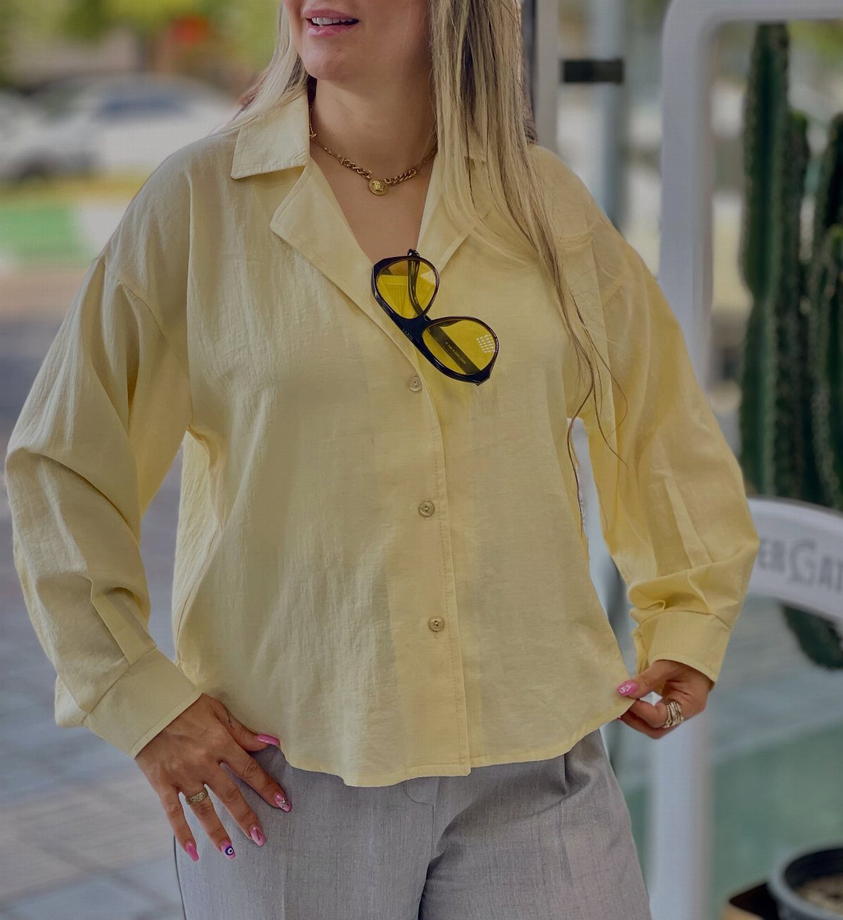 Woman wearing a pale yellow long-sleeve button-down shirt and light grey trousers.