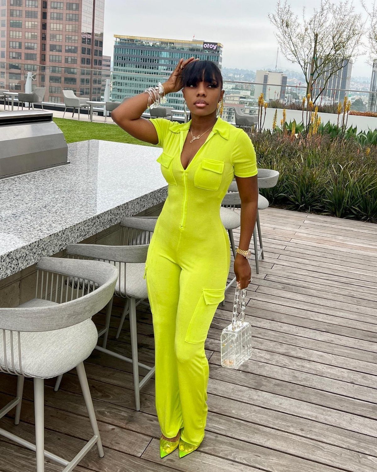 Woman in neon yellow short-sleeved jumpsuit posing on a city rooftop deck.