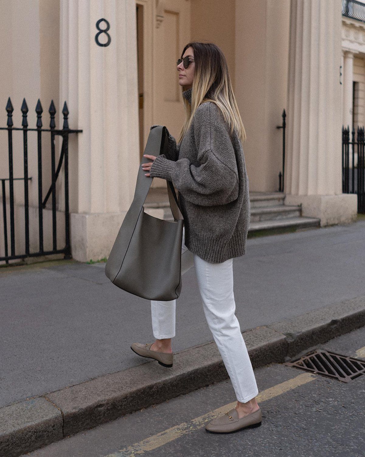 70's Inspired Outfits: 13 Retro Looks to Try Right Now 10 Woman in a chunky grey knit sweater and white trousers on a city street.