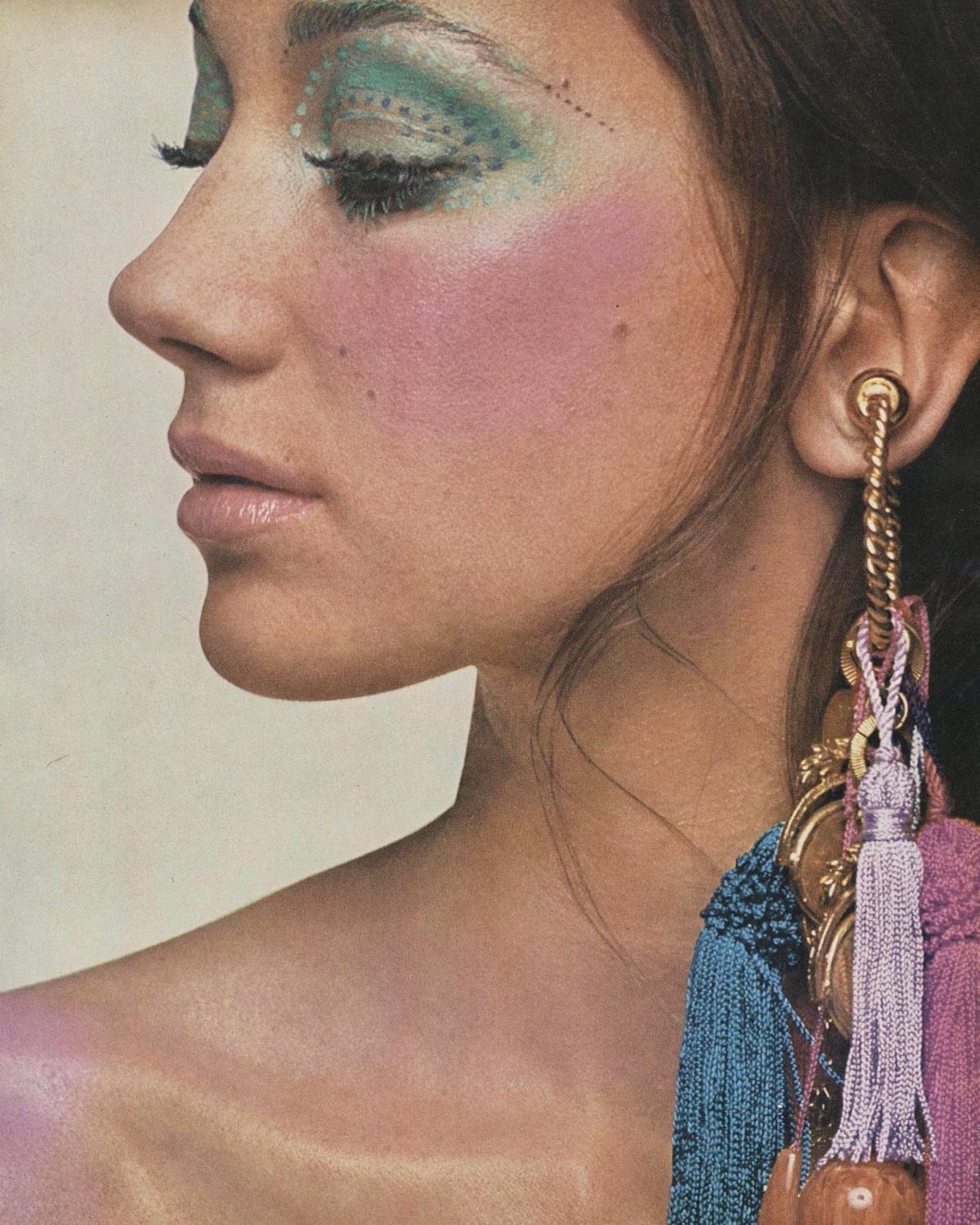 70's Inspired Outfits: 13 Retro Looks to Try Right Now 12 Woman with green eyeshadow and pink blush wearing a large tassel earring.
