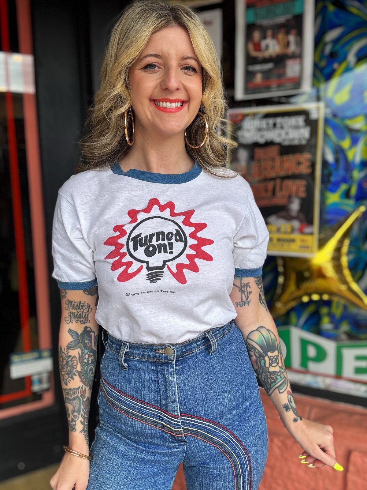 70's Inspired Outfits: 13 Retro Looks to Try Right Now 13 Woman wearing a white vintage graphic t-shirt and high-waisted blue denim jeans.
