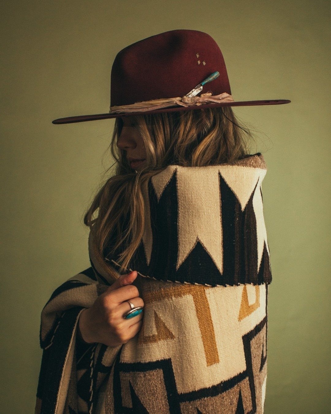 70's Inspired Outfits: 13 Retro Looks to Try Right Now 9 Woman wearing a wide-brimmed burgundy felt hat and a patterned bohemian blanket.