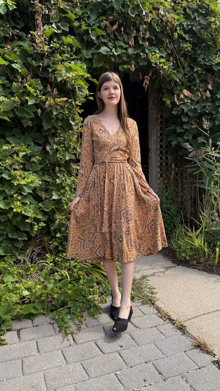 70's Inspired Outfits: 13 Retro Looks to Try Right Now 2 Woman wearing a brown patterned wrap dress and black platform heels by a green wall.
