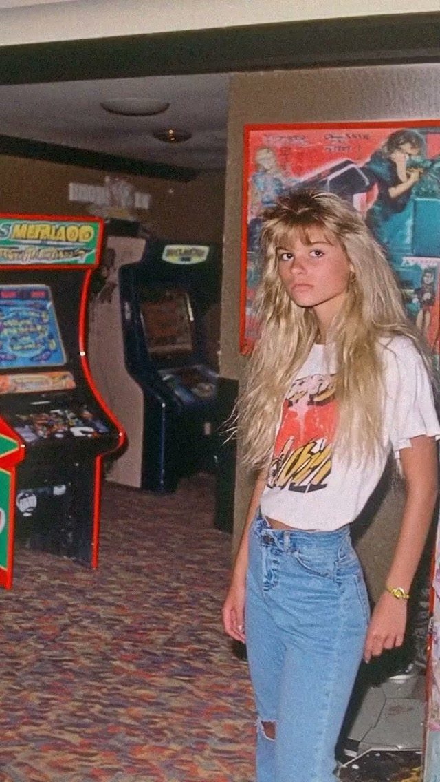 80s Inspired Outfits: 8 Bold Looks to Recreate the Decade 8 Young woman with big blonde hair wearing a graphic tee and high-waisted jeans.