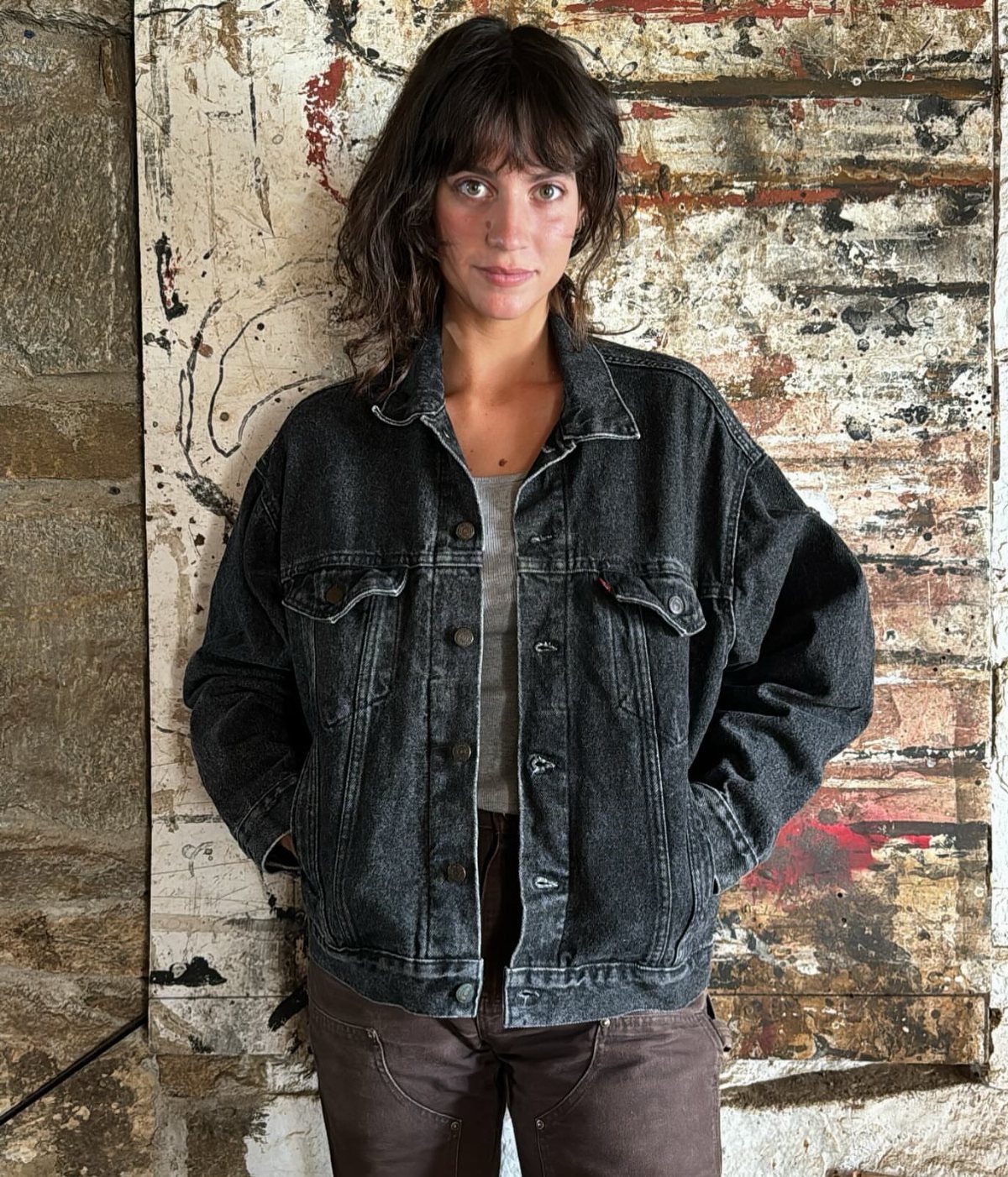 80s Inspired Outfits: 8 Bold Looks to Recreate the Decade 2 Woman wearing an oversized black denim jacket posing against a rustic textured wall.