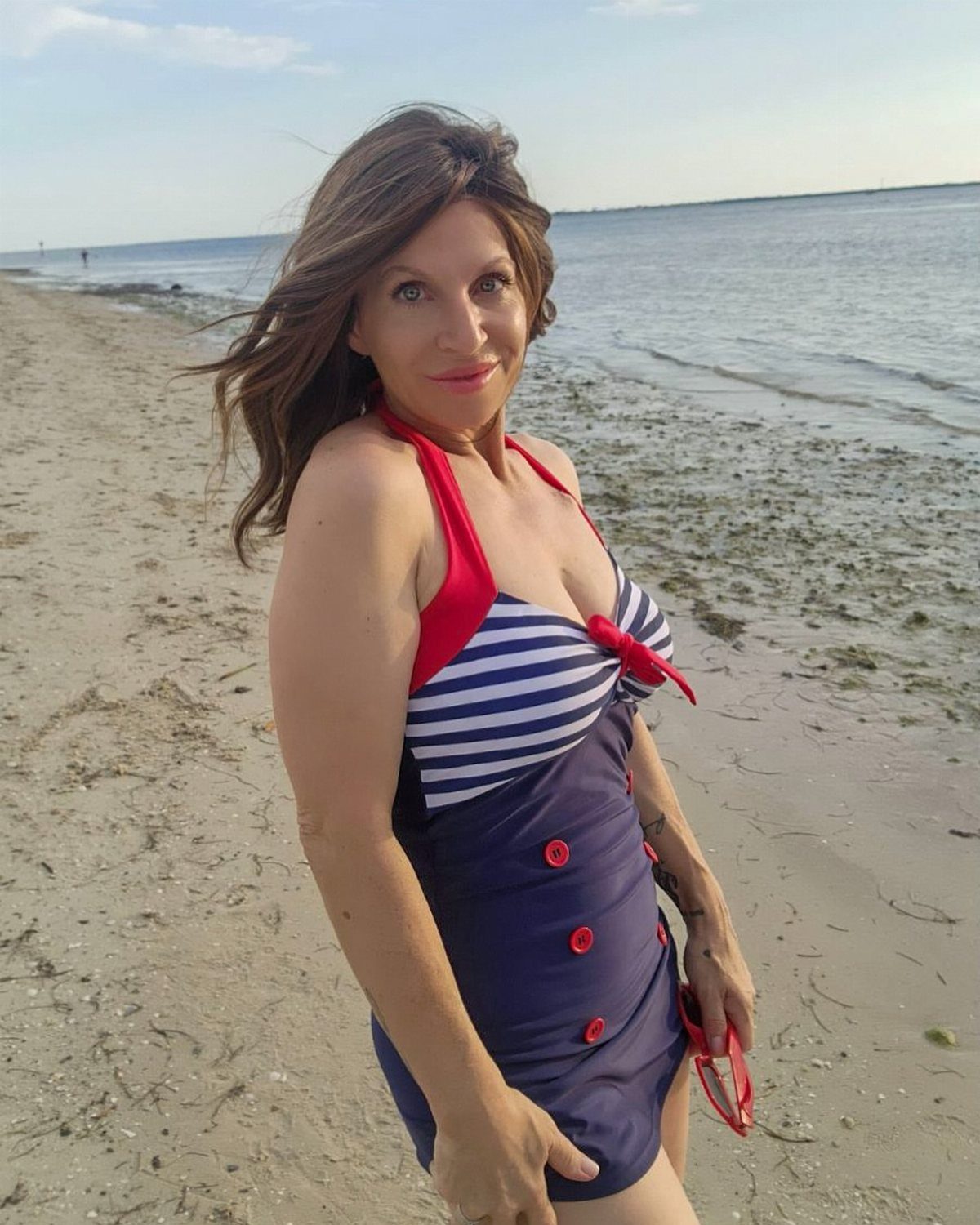 80s Inspired Outfits: 8 Bold Looks to Recreate the Decade 5 Woman in a retro navy and red striped one-piece swimsuit on a beach.