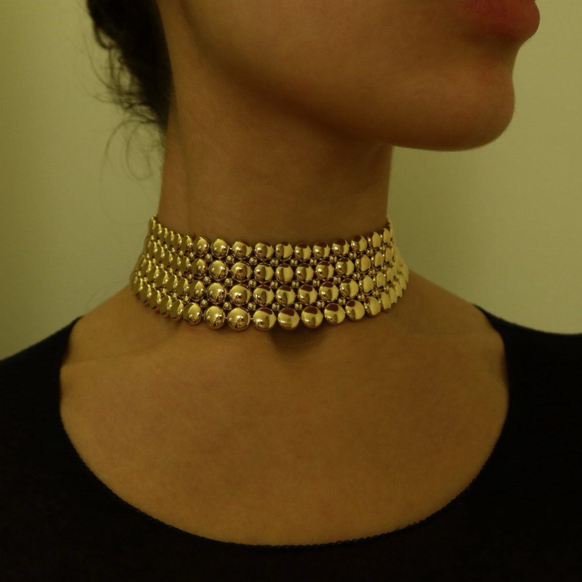 Gold beaded choker necklace worn around a person's neck with a black shirt.