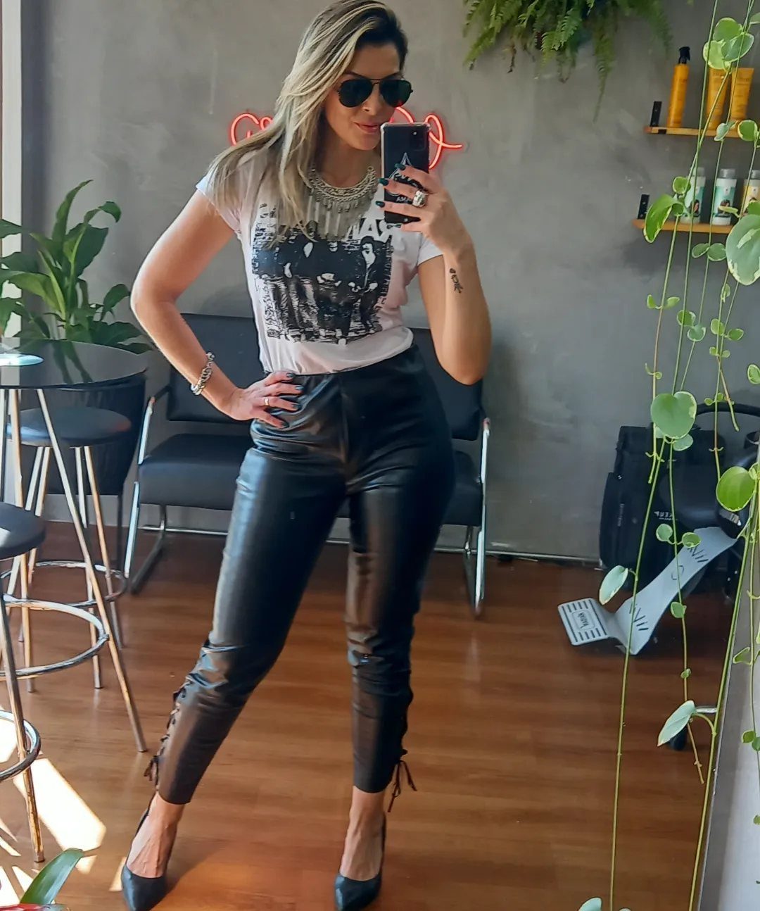 Woman in white graphic tee and black leather pants posing for a mirror selfie.