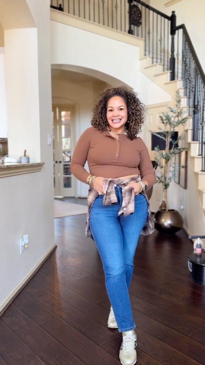 Woman wearing a brown top, blue jeans, and a plaid shirt tied around her waist.