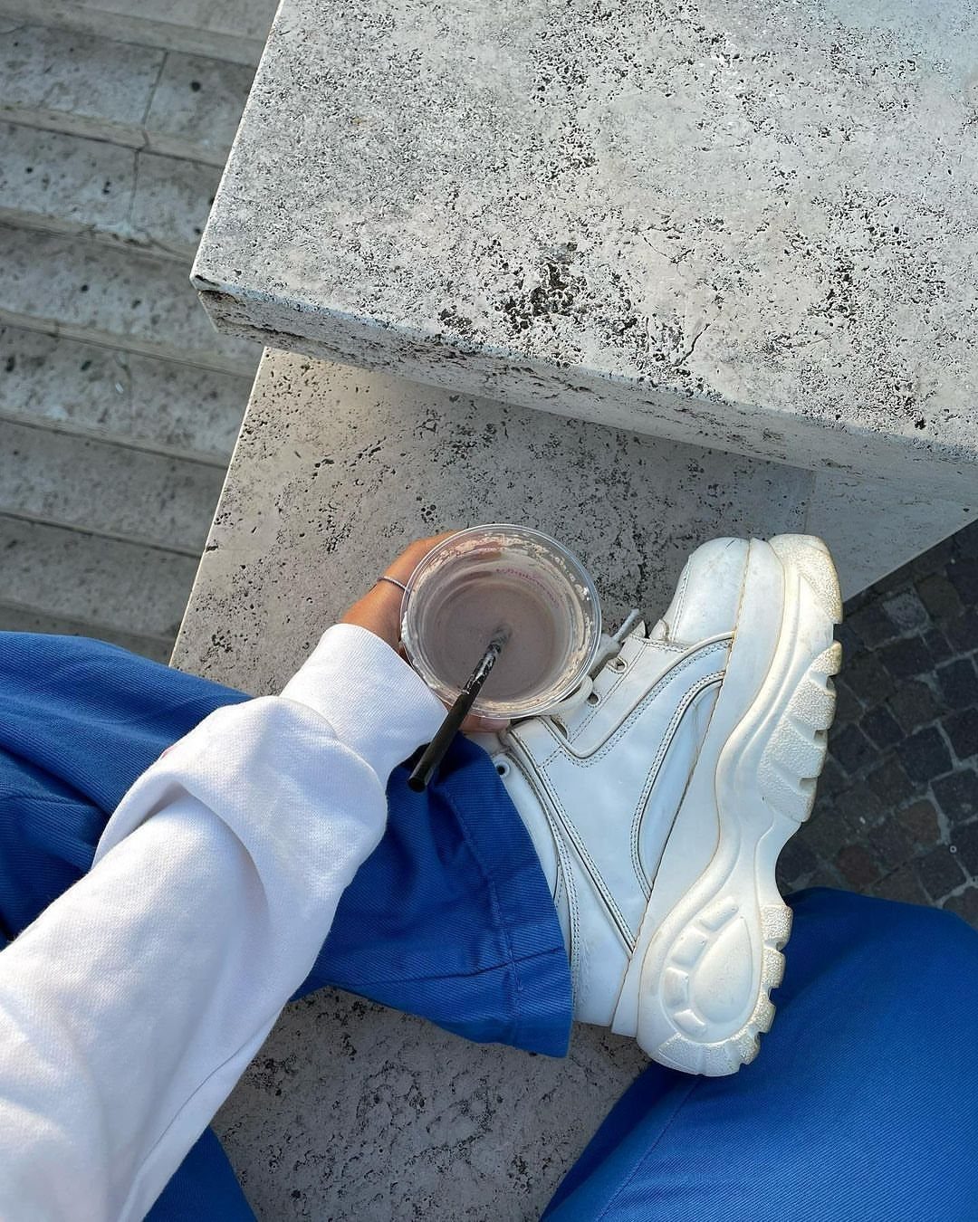 White chunky platform sneaker worn with bright blue trousers on stone steps.