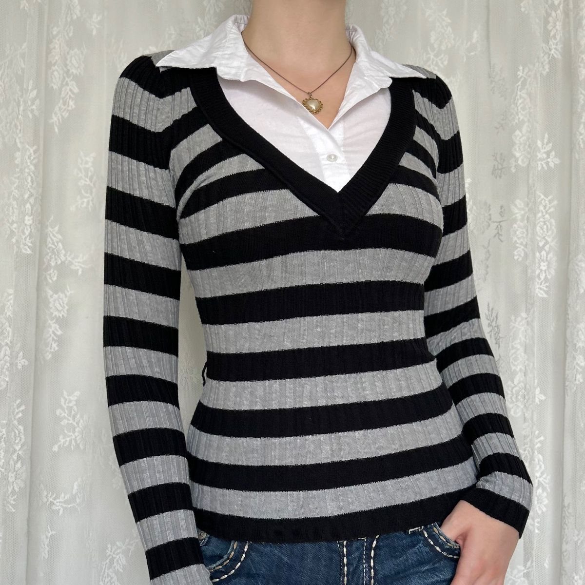 Person wearing a black and grey striped sweater over a white collared shirt.