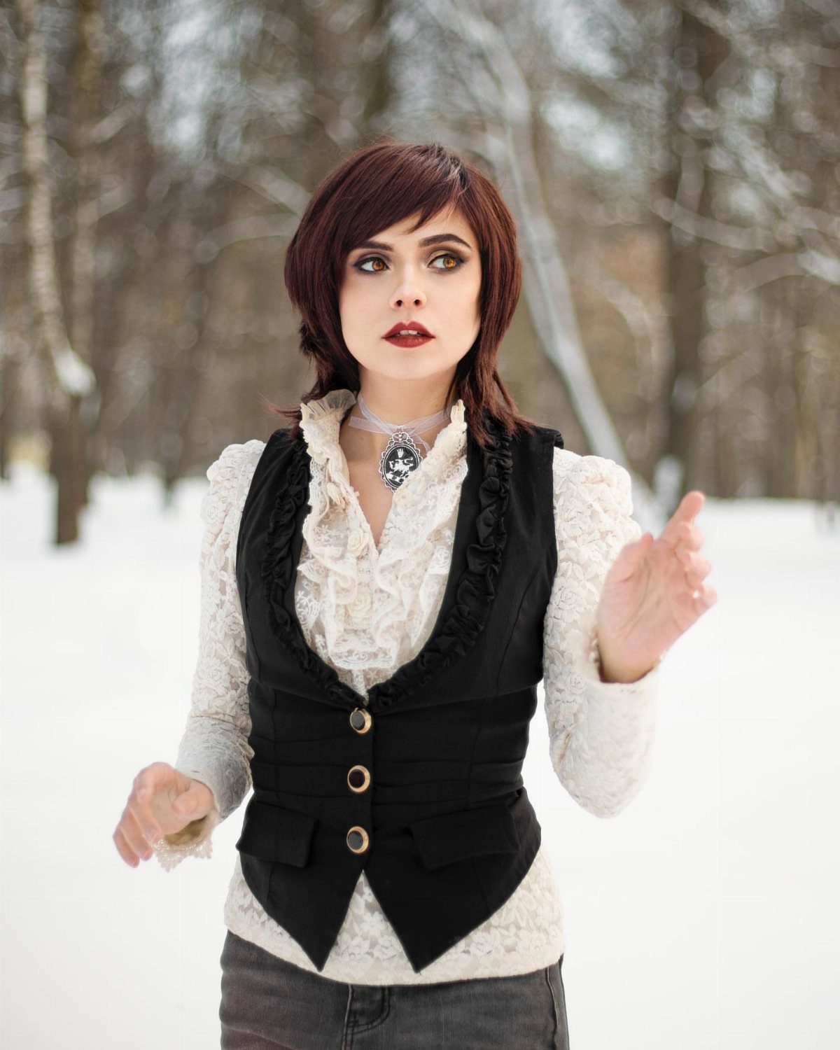 Woman wearing a white ruffled blouse, black vest, and grey skinny jeans in snow.