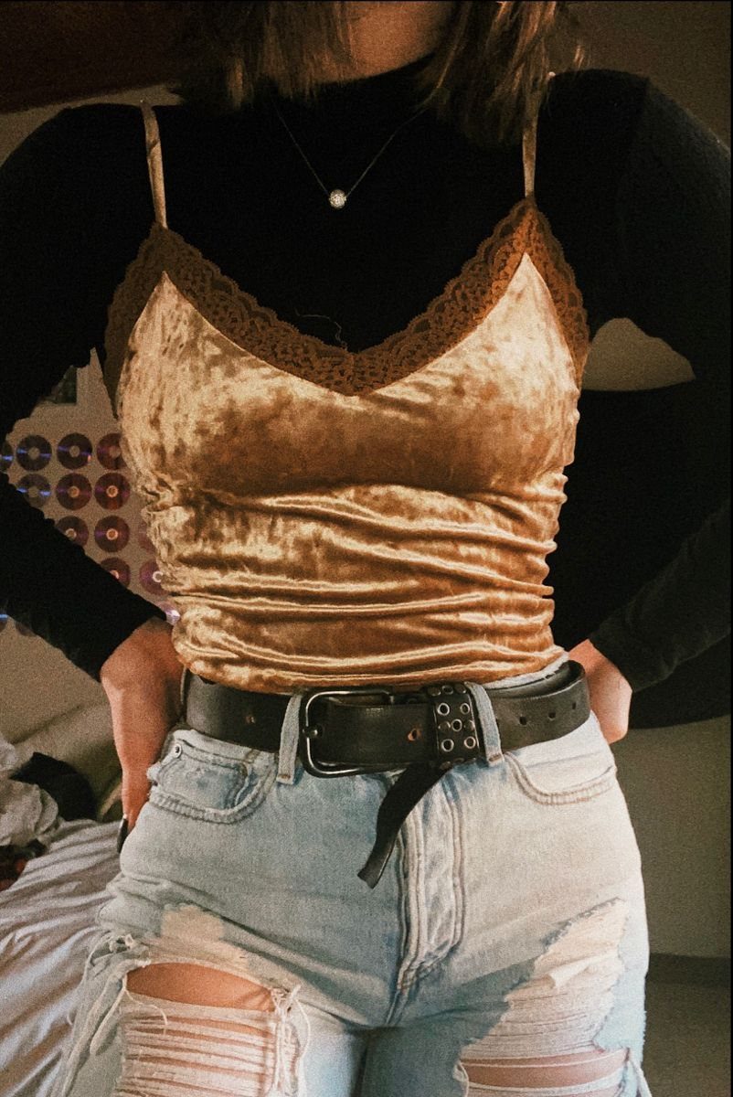 Person wearing gold velvet lace top with black shirt and ripped denim jeans.