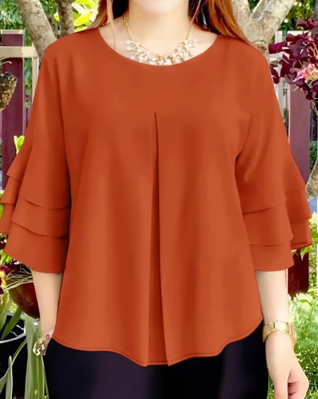 Apple Body Shape Outfits That Flatter Your Figure (9 Ideas) 3 Burnt orange flowy blouse with tiered bell sleeves and a gold necklace.