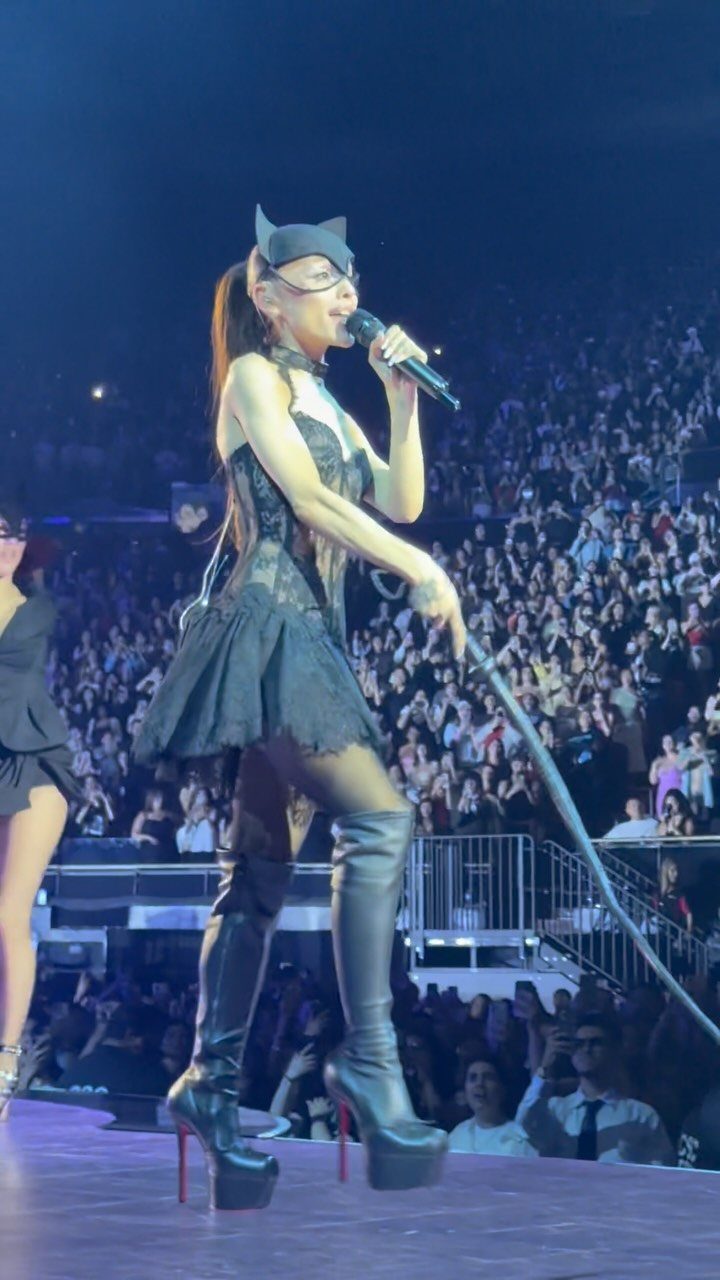 Ariana Grande Concert Outfits: 12 Looks for 2026 Shows 4 Ariana Grande on stage wearing a black lace corset and short flared skirt.