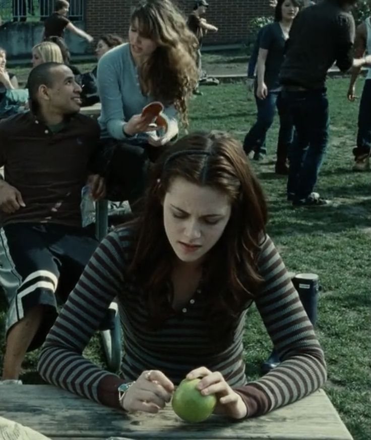 Bella Swan Outfits: 10 Iconic Looks from the Twilight Saga 10 Woman in a striped long-sleeve shirt sitting at a picnic table with an apple.
