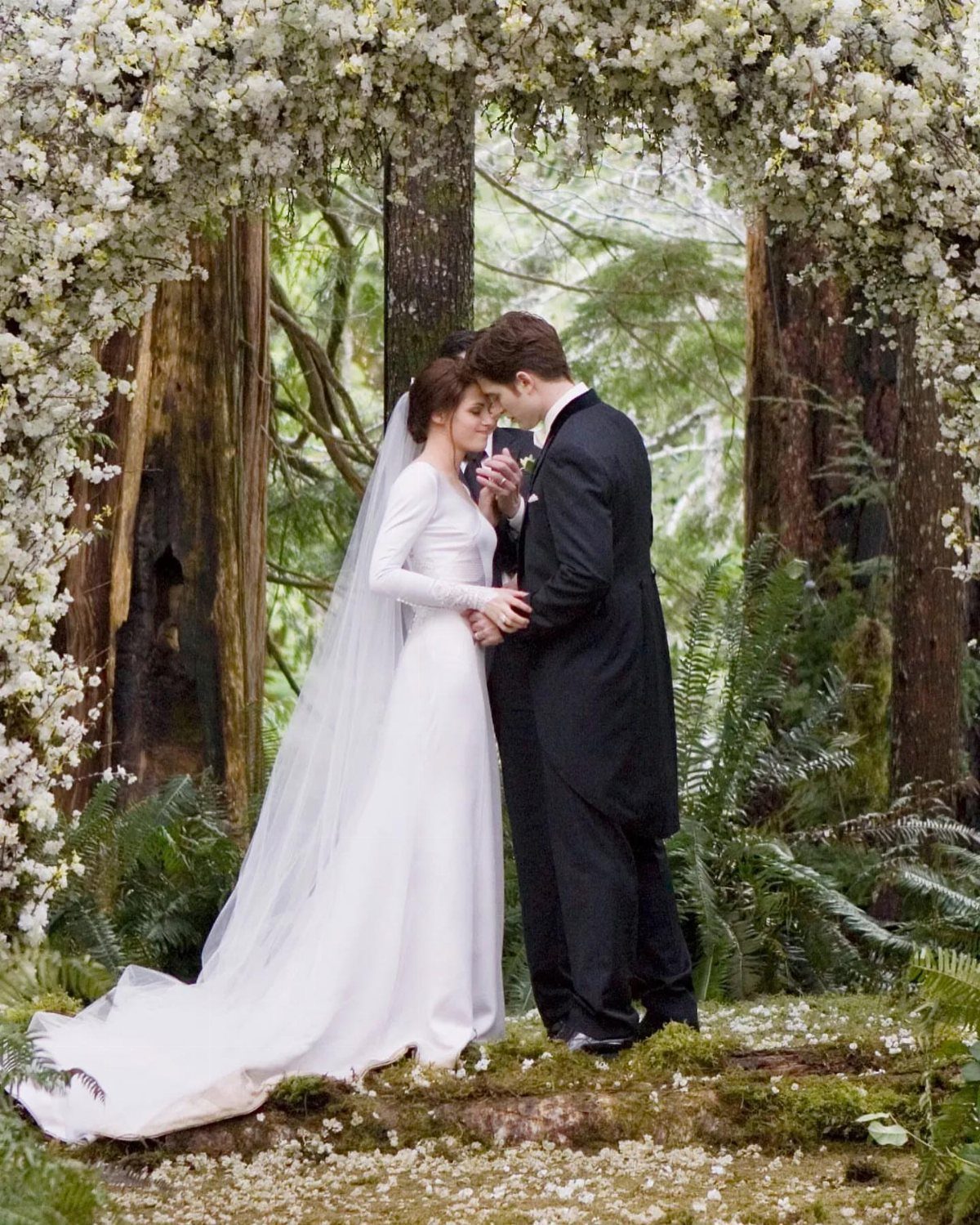 Bella Swan Outfits: 10 Iconic Looks from the Twilight Saga 3 Bride in long-sleeve white wedding dress and groom in black tuxedo under floral arch