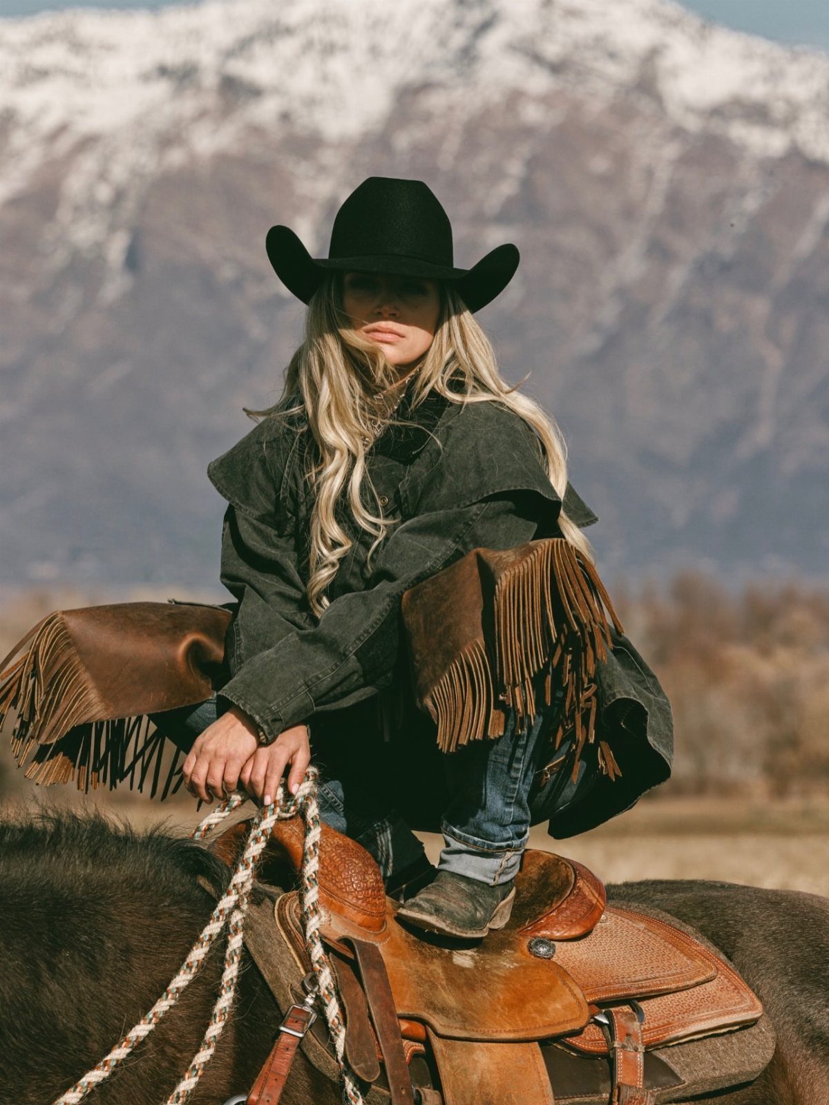 Beth Dutton Outfits: 12 Looks from Yellowstone's Style Icon 8 Blonde woman in black cowboy hat and fringed jacket sitting on a horse.