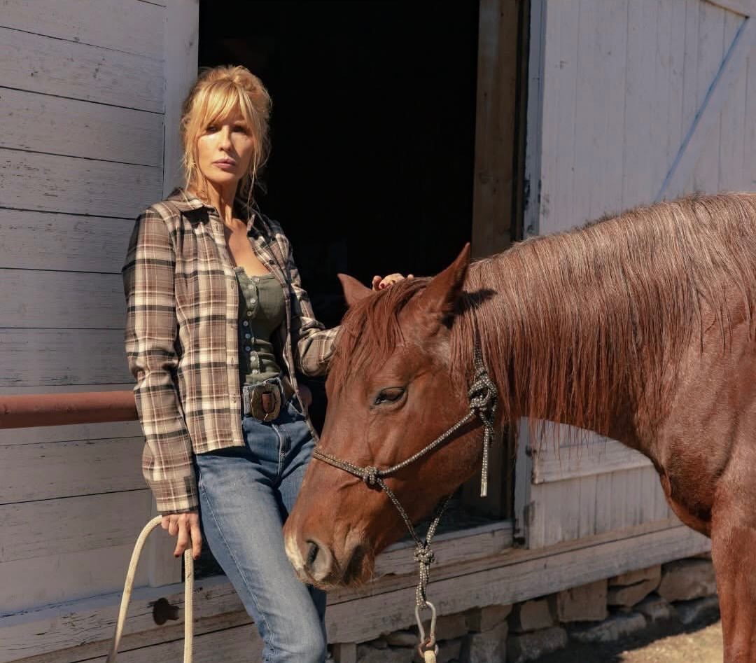 Beth Dutton Outfits: 12 Looks from Yellowstone's Style Icon 1 Woman in plaid shirt and blue jeans standing beside a brown horse.