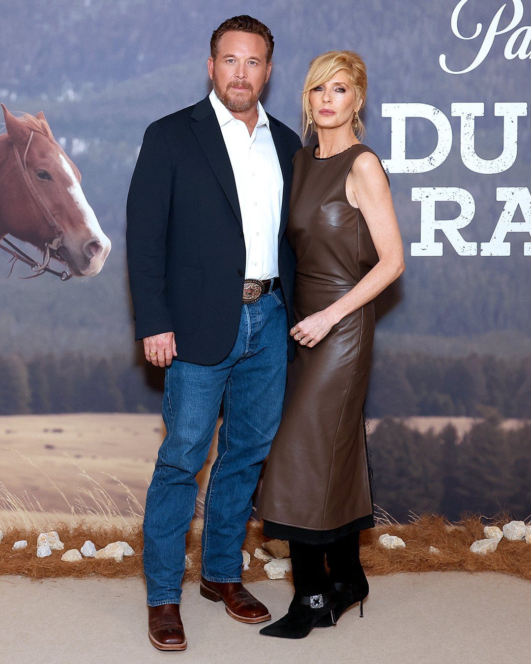 Beth Dutton Outfits: 12 Looks from Yellowstone's Style Icon 12 Man in blazer and woman in brown leather dress posing together outdoors.