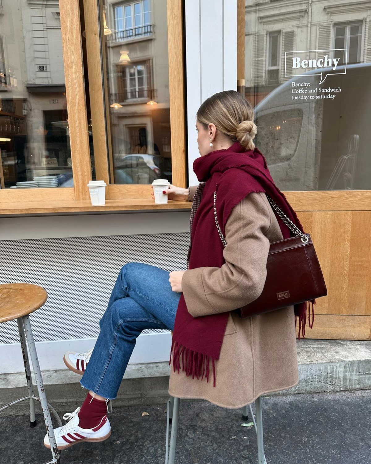 7 Burgundy Outfits for Women to Wear This Season 3 Woman in tan coat and burgundy scarf sitting at a cafe with burgundy bag