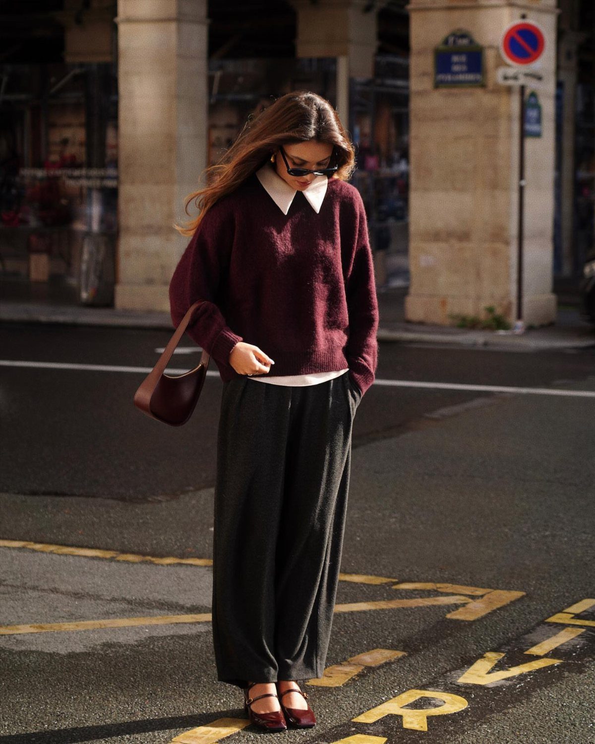 7 Burgundy Outfits for Women to Wear This Season 7 Woman wearing a burgundy sweater, white collared shirt, and wide-leg dark grey trousers.