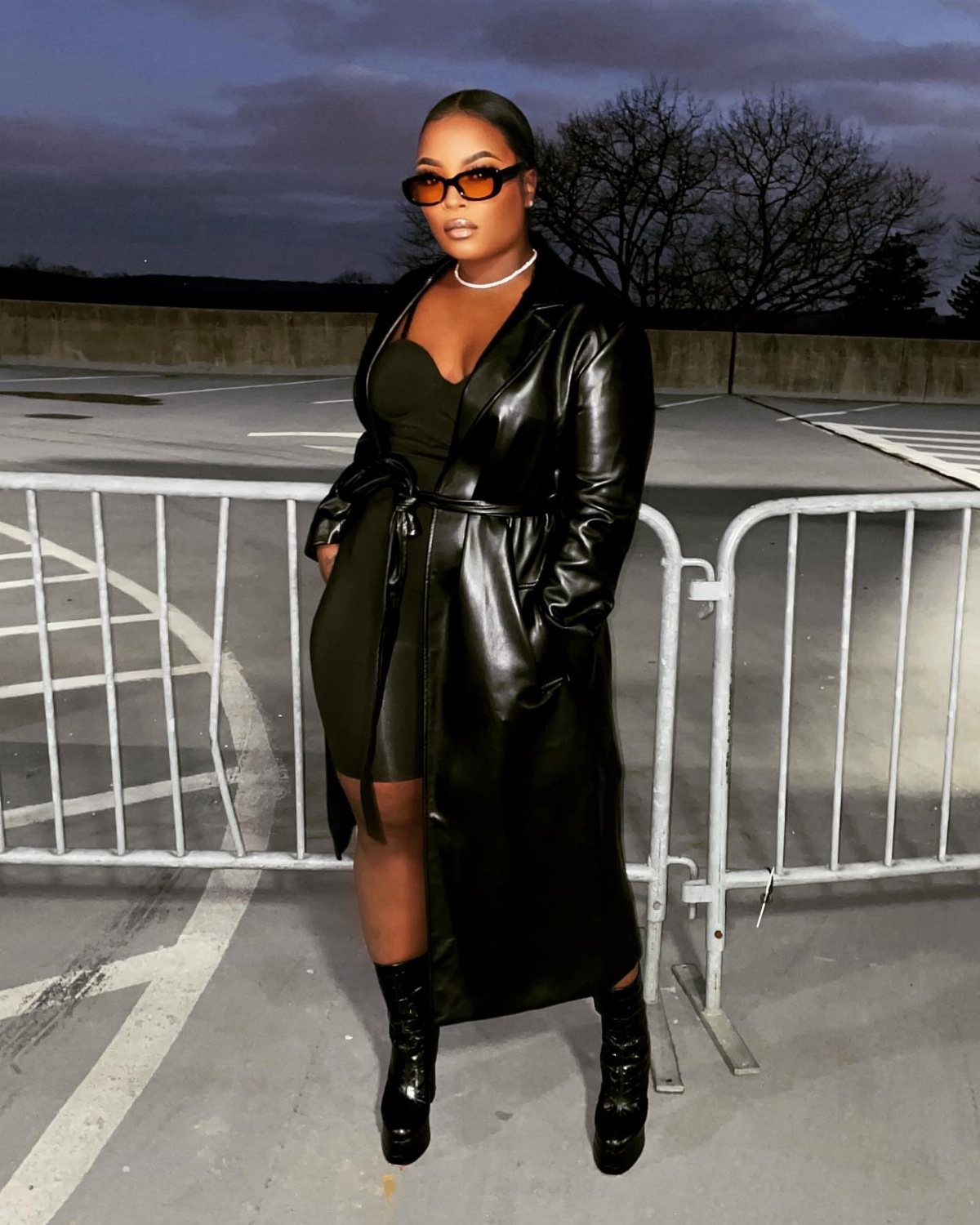 Cardi B Concert Outfits: 9 Bold Looks to Turn Heads 6 Woman in a black faux leather coat and mini dress posing in a parking lot.