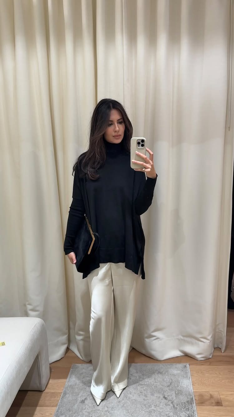 13 Carolyn Bessette Outfits You Can Actually Wear Today 12 Woman wearing an oversized black turtleneck sweater and wide-leg white trousers.