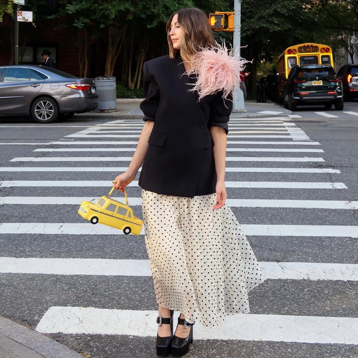 Carrie Bradshaw Outfits: 11 Iconic Looks to Recreate 9 Woman in a black blazer and polka-dot skirt holding a taxi-shaped handbag.