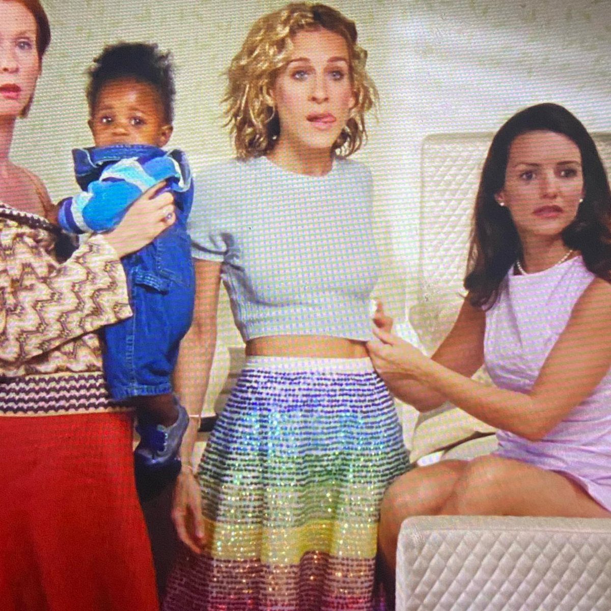 Carrie Bradshaw Outfits: 11 Iconic Looks to Recreate 11 Woman in a blue cropped shirt and colorful sequined skirt standing with friends.