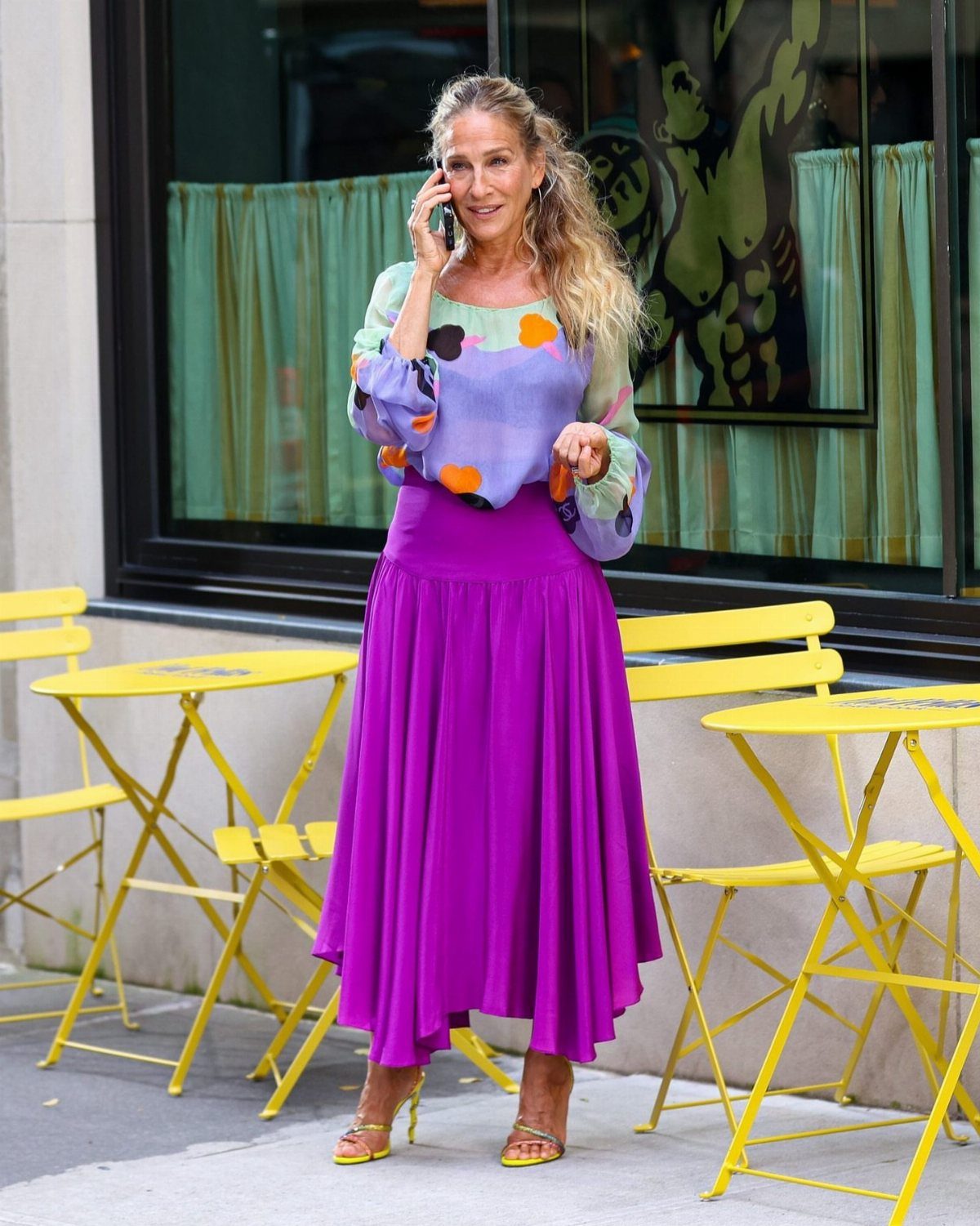 Carrie Bradshaw Outfits: 11 Iconic Looks to Recreate 1 Woman wearing a colorful patterned blouse and long purple skirt with yellow heels.