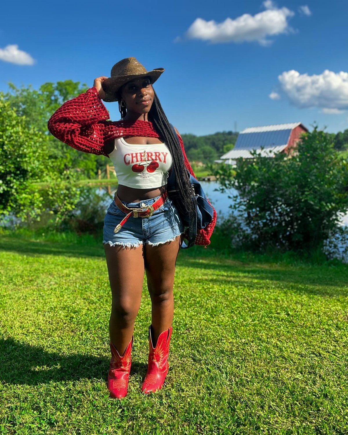 14 Coastal Cowgirl Outfits for Breezy Western Beach Style 12 Woman in a red crochet shrug, denim shorts, and red cowboy boots in a field.