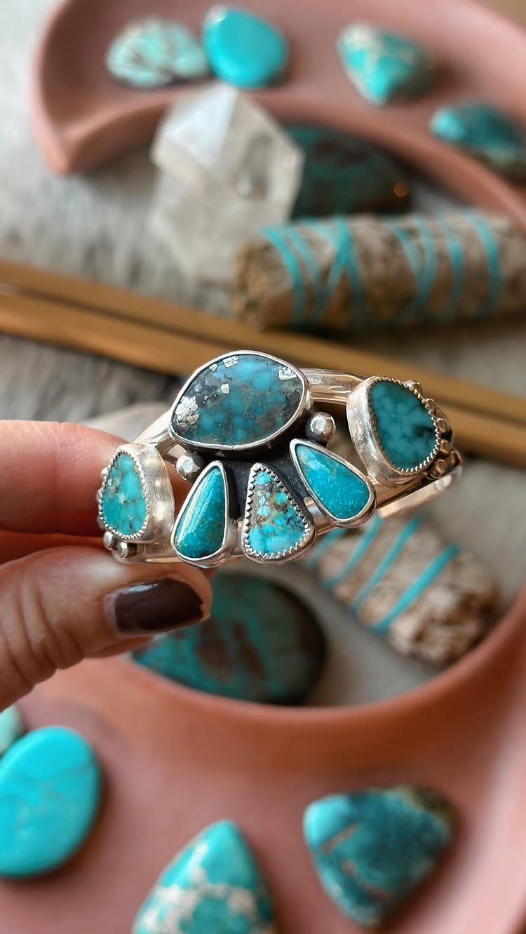 14 Coastal Cowgirl Outfits for Breezy Western Beach Style 3 Silver ring with turquoise stones held against a background of turquoise gems.