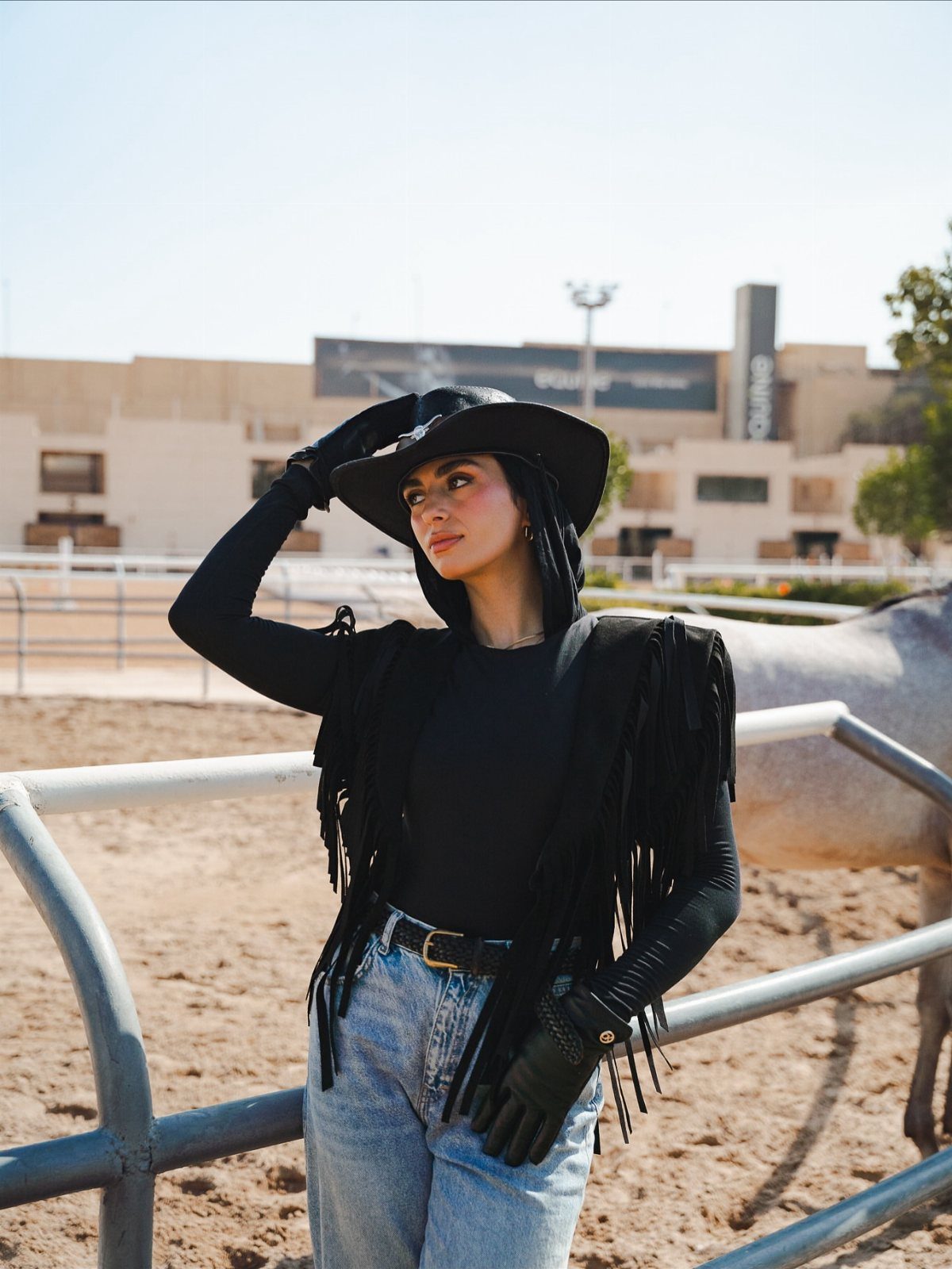 11 Comfortable Concert Outfits You'll Want to Wear in 2026 5 Woman wearing a black fringe vest, black hat, and blue jeans outdoors.