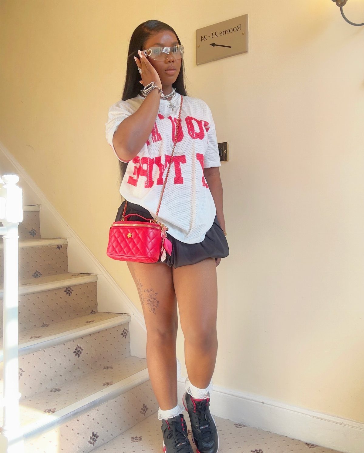 11 Comfortable Concert Outfits You'll Want to Wear in 2026 6 Woman in white graphic tee and black skirt posing on carpeted stairs.