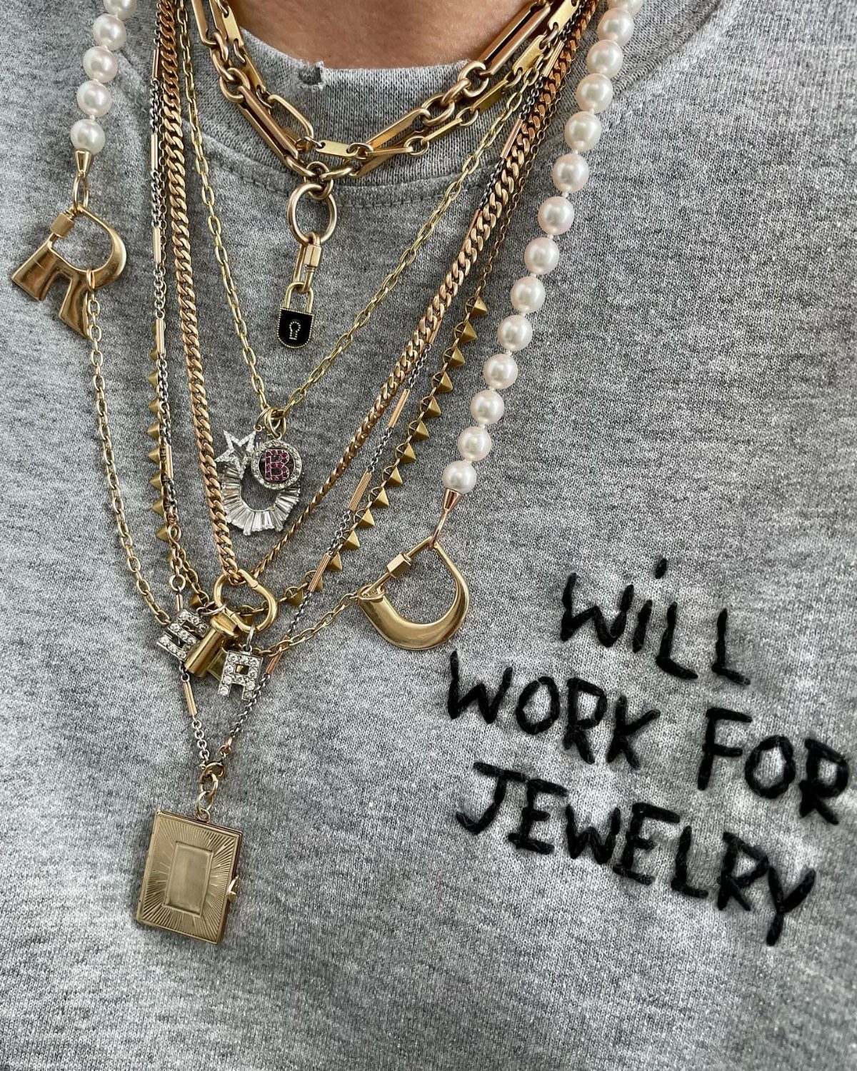 11 Comfortable Concert Outfits You'll Want to Wear in 2026 8 Layered gold and pearl necklaces worn over a grey graphic t-shirt.