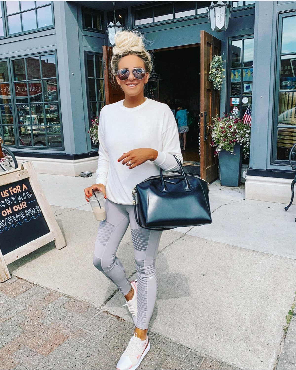 11 Comfortable Concert Outfits You'll Want to Wear in 2026 9 Woman in white long-sleeved shirt and grey leggings standing outside a shop.