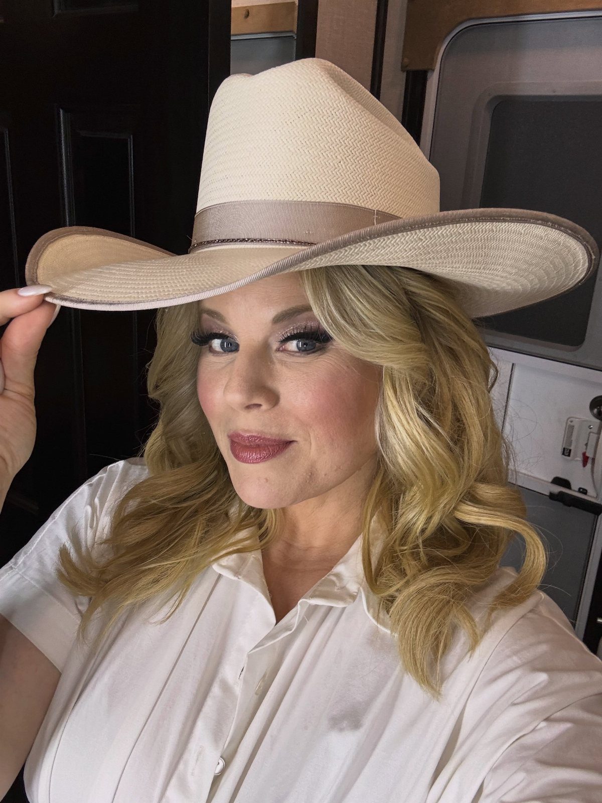 11 Comfortable Concert Outfits You'll Want to Wear in 2026 3 Woman wearing a wide-brimmed beige straw hat and a white button-down shirt.