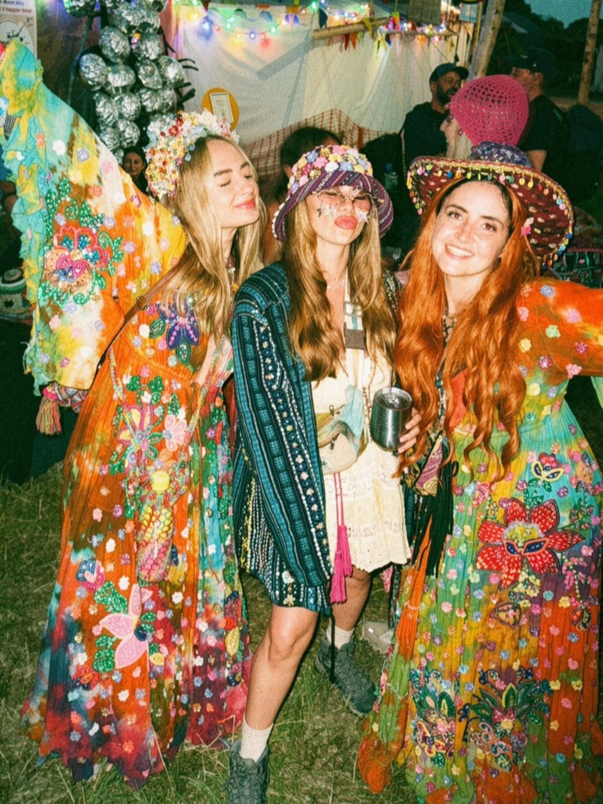 Concert Outfits for Women: 8 Looks That Work for Any Venue 8 Three women in colorful bohemian dresses and hats posing at an outdoor festival.