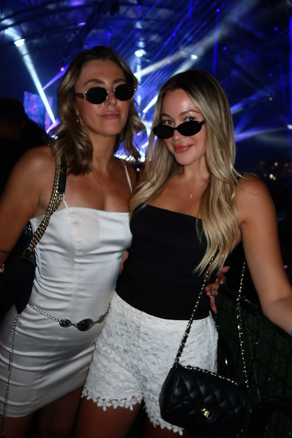 Concert Outfits for Women: 8 Looks That Work for Any Venue 4 Two women wearing stylish black sunglasses and concert attire under blue lights.