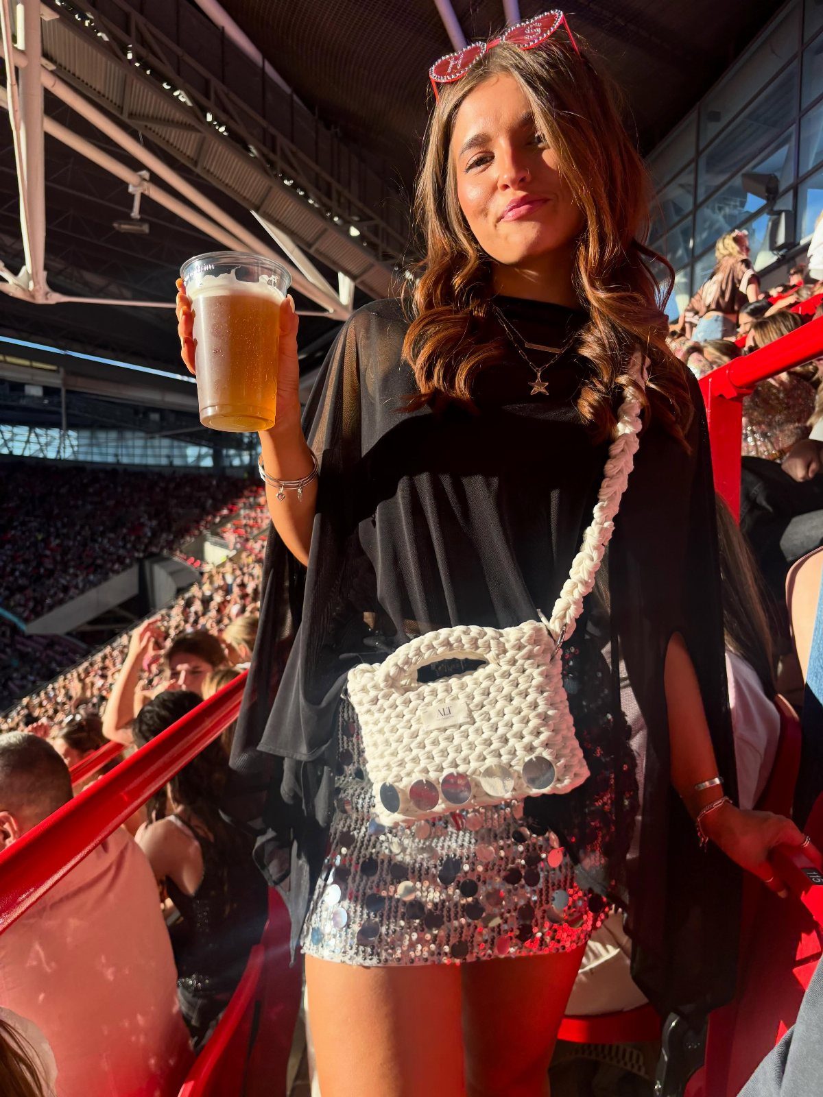 Concert Outfits for Women: 8 Looks That Work for Any Venue 7 Woman wearing a white crossbody bag and layered necklaces at a concert stadium.