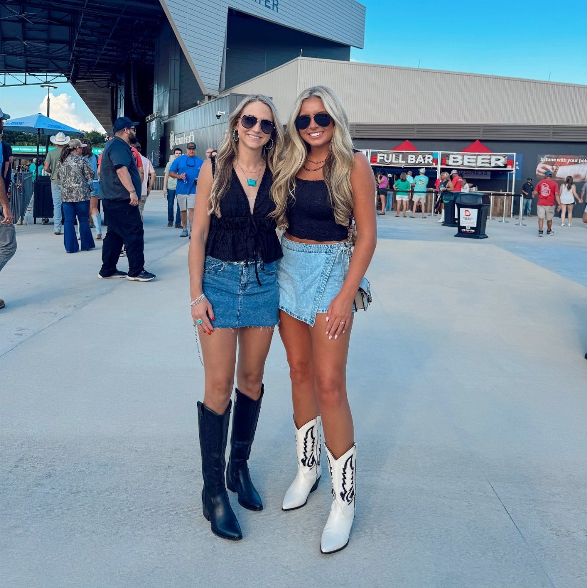 Concert Outfits for Women: 8 Looks That Work for Any Venue 6 Two women wearing denim skirts and cowboy boots at an outdoor concert venue.