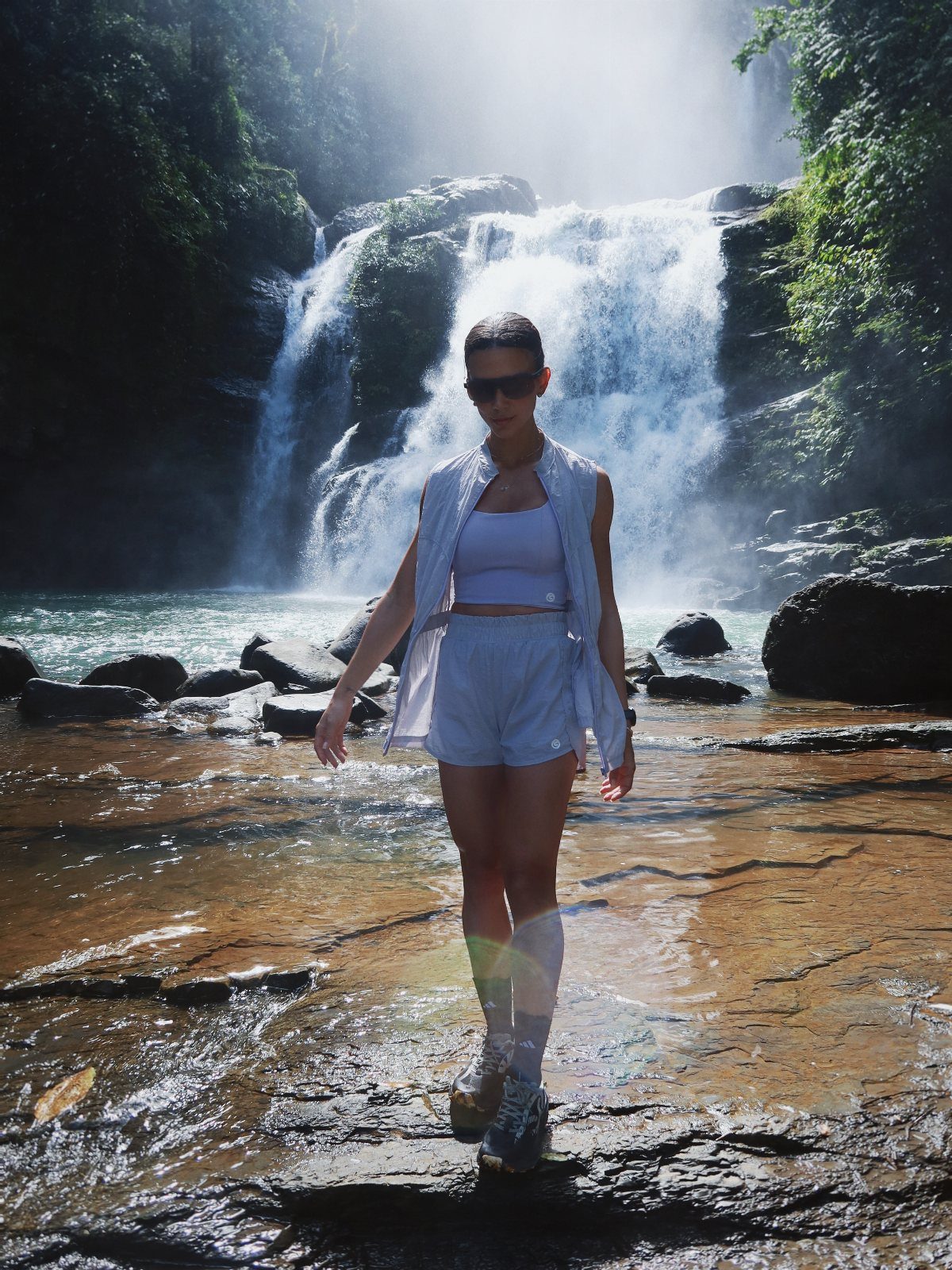 Costa Rica Outfits: 10 Ideas for Your Trip 7 Woman in white summer outfit and hiking boots posing before a tropical waterfall.