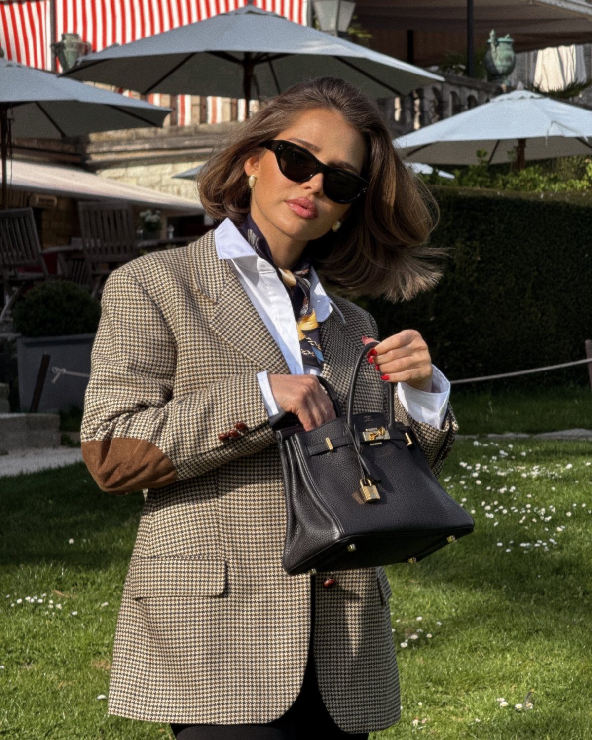 7 Country Club Outfits That Balance Style and Tradition 1 Woman in a checkered blazer and white shirt holding a black leather handbag.